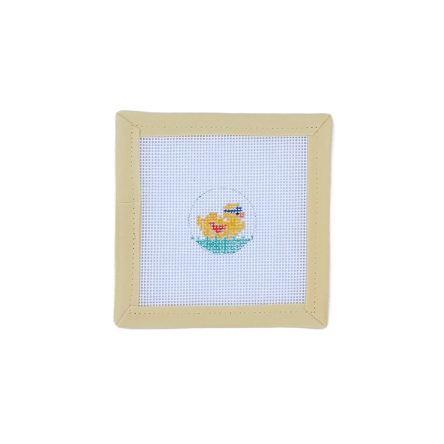 Cross-stitched design of a yellow duck in a green pond on white fabric with a beige frame.